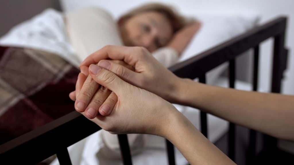 Daughter supporting mother lying on hospital bed